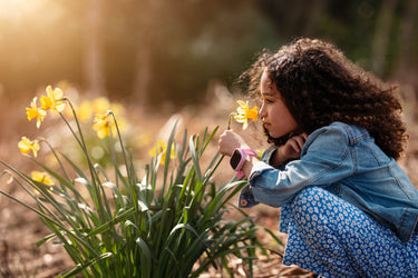 Young girl smelling a flower with a X6Play kids smartwatch from Xplora in purple 